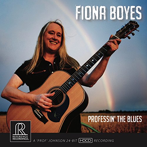Fiona Boyes smiling, holding an acoustic guitar against a rainbow backdrop.