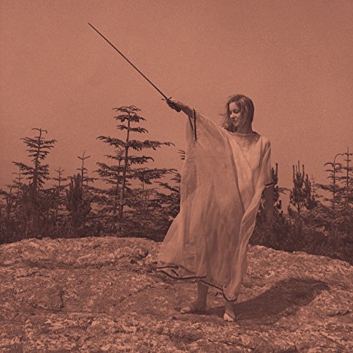 Person in white robe holding a stick, forested landscape background.
