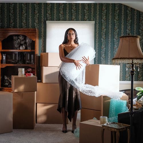 Woman in gold dress holding bubble wrap, surrounded by cardboard boxes.