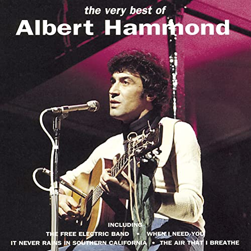 Albert Hammond playing an acoustic guitar and singing into a microphone on stage.