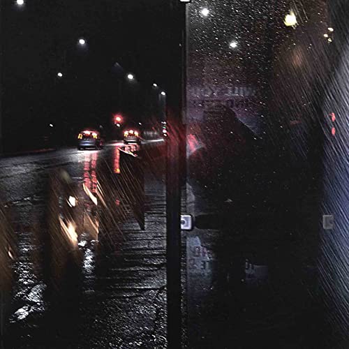 Rain-streaked window view of a dark, wet city street with vehicle lights.