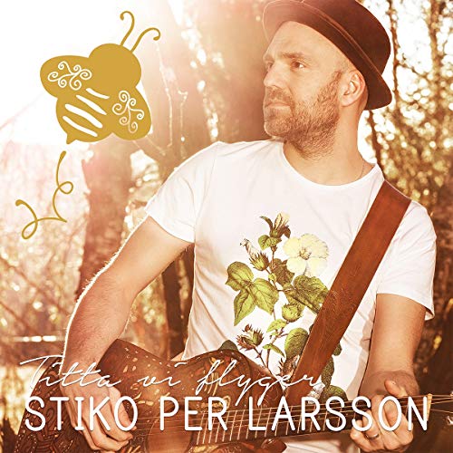 Man in hat and white t-shirt with floral design playing guitar outdoors.