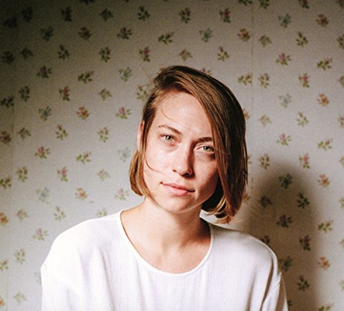 Portrait of Anna Burch, a woman with short hair, against floral wallpaper.
