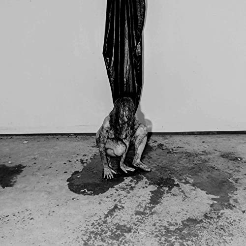 Black and white image of a person crouching in a wet space.
