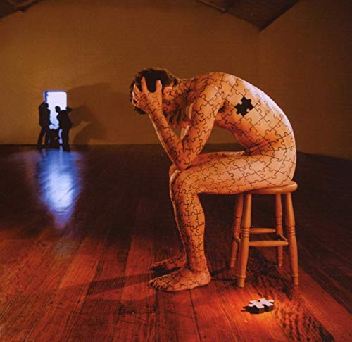 Man with puzzle-piece skin sits on stool in a room.