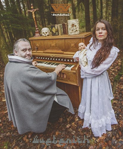 A man and woman with a doll by a piano in a forest.