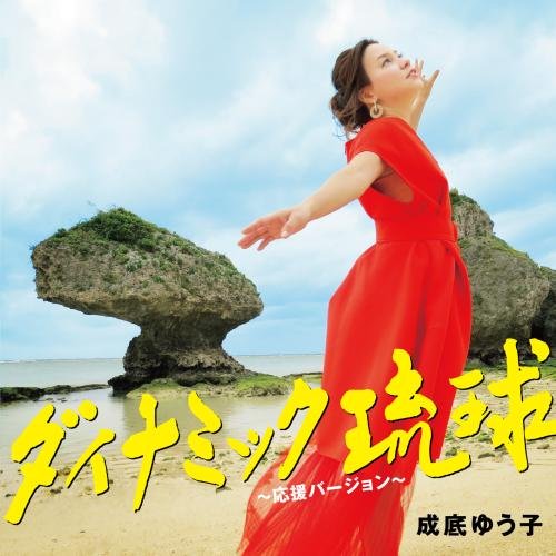 Woman in red dress on a beach with a rock formation.