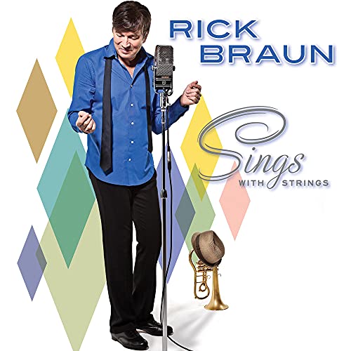 Rick Braun in a blue shirt standing by a microphone and trumpet.