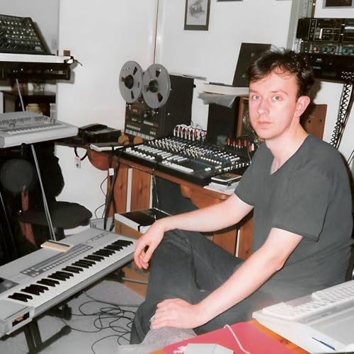 Man seated in a home studio surrounded by audio equipment.