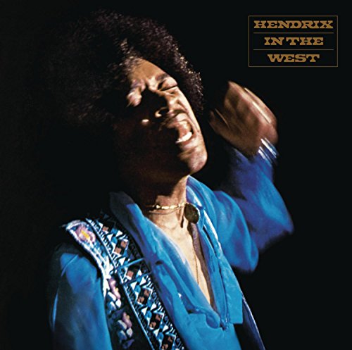 Jimi Hendrix singing on stage, wearing a blue shirt, against a dark background.