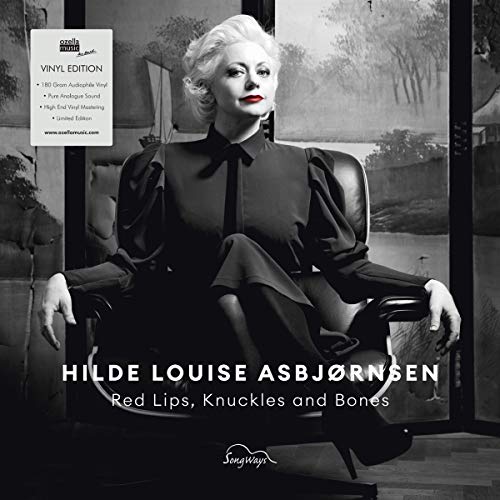 Woman with platinum hair in black clothing seated in a chair.