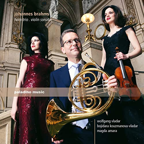 Three musicians with a French horn, violin, and ornate background.