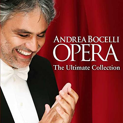 Andrea Bocelli smiling in a tuxedo against a red curtain background.