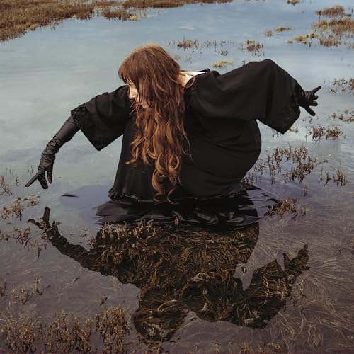 Woman in black dress sitting in shallow water, long hair flowing.