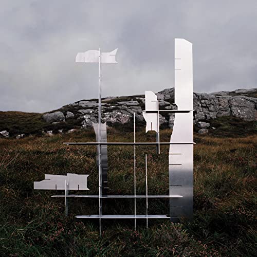 Silver abstract sculpture in a grassy field with a cloudy sky.