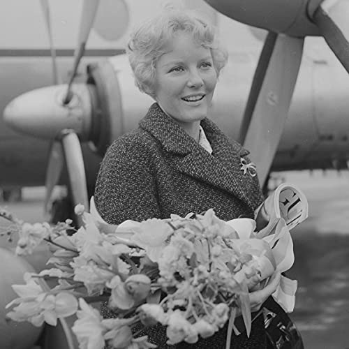 Black and white portrait of Petula Clark holding flowers near an airplane.