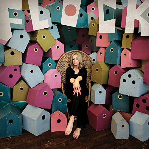 Woman sitting in chair surrounded by colorful, patterned birdhouses.