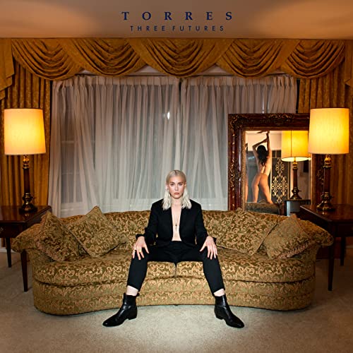 Woman seated on a patterned couch in a vintage-style room.