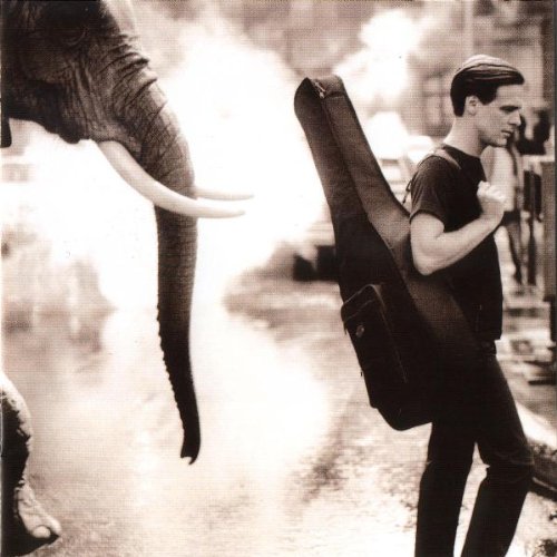 Black and white photo of Bryan Adams with an elephant, carrying a guitar case.