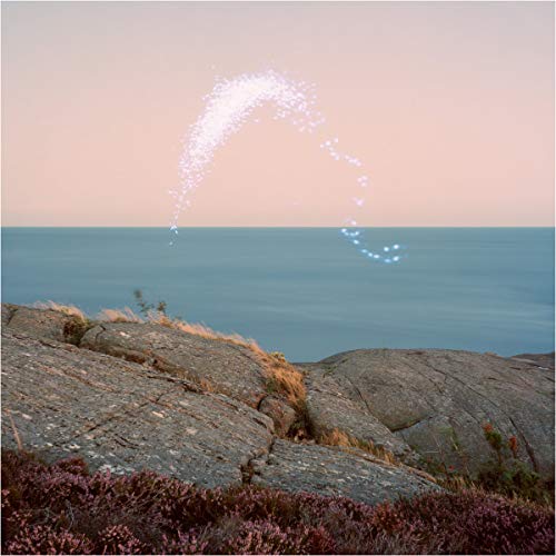 Coastal rocks with a spray of light over the ocean under a pink sky.