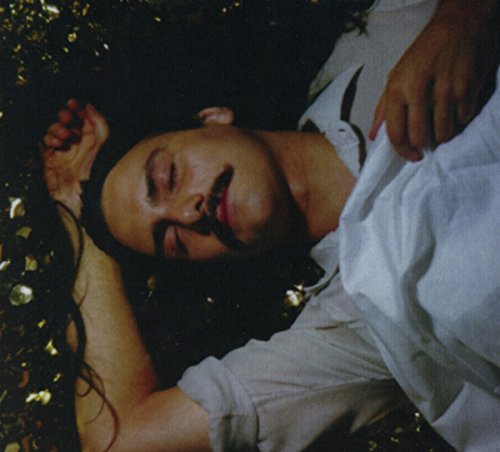 Man with dark markings on face lies amongst gold confetti.