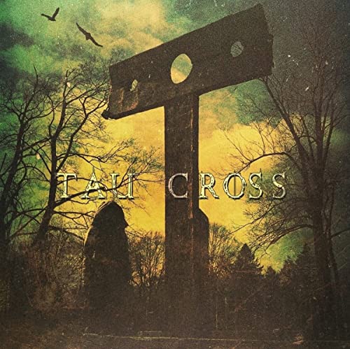 Dark forest scene with a large T-shaped cross and hooded figure at sunset.