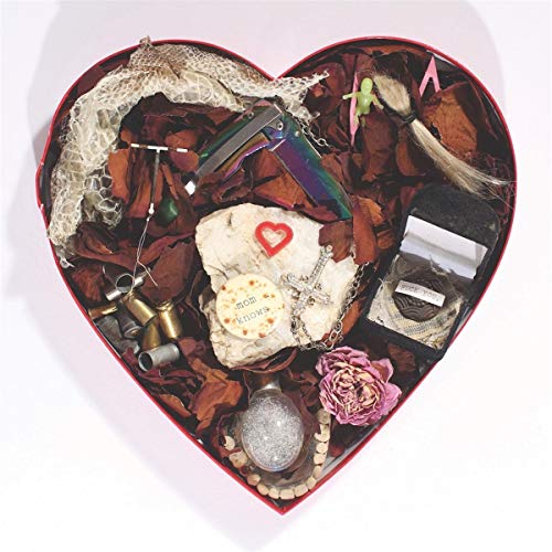 Heart-shaped box filled with diverse objects including a gun and flowers.