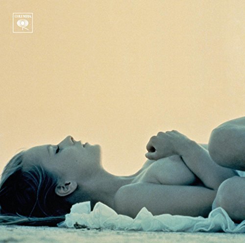 A woman lies on her side on a sandy surface against a pale background.