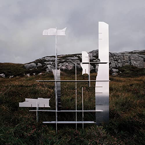 Silver abstract sculpture resembling a ship in a grassy, rocky landscape.