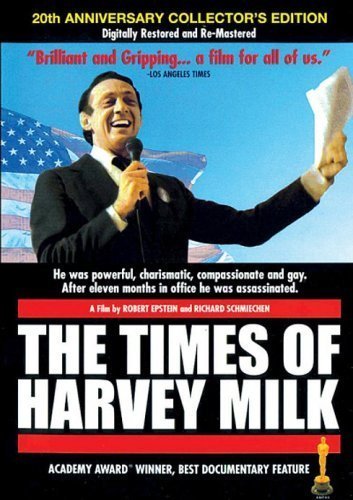 Harvey Milk speaking into a microphone with an American flag backdrop.