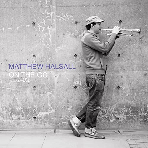 Matthew Halsall playing trumpet against a textured concrete wall.