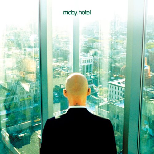Bald man in suit views a bright, hazy cityscape through large windows.