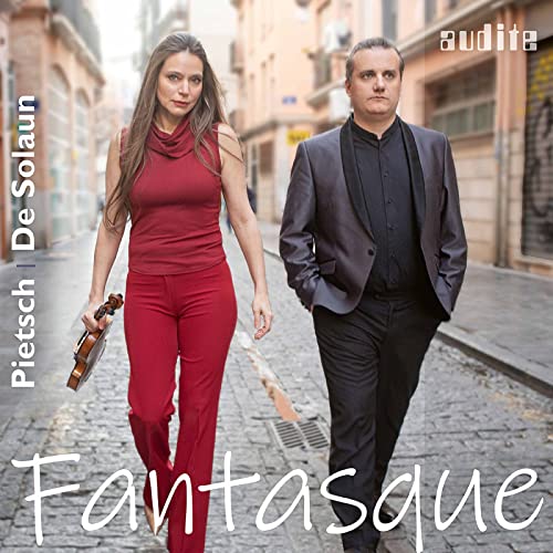 Two musicians, a woman with a violin and a man, walking on a street.