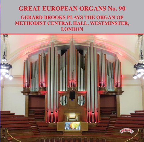 Large pipe organ in a hall with red seating, illuminated by red light.