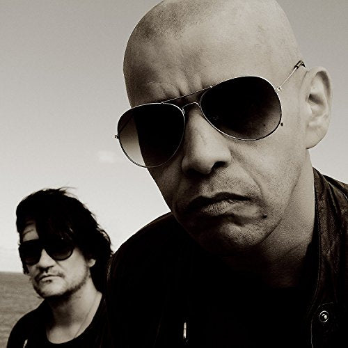 Two men in sunglasses, one bald, in a sepia-toned portrait.