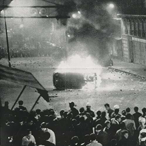 Black and white photo of a burning car surrounded by a crowd.