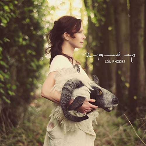 Woman in a white dress holding a stuffed ram in a forest.
