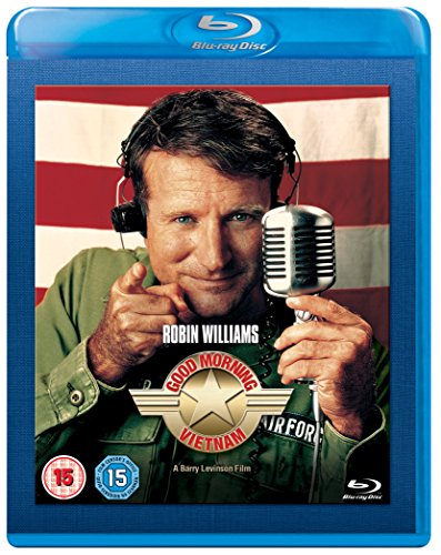 Robin Williams wearing headphones and holding a microphone in front of an American flag.