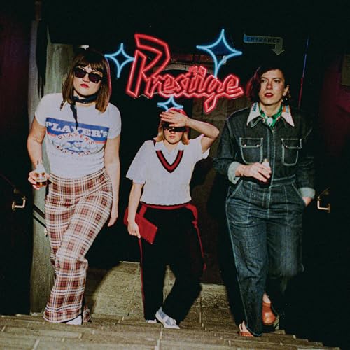 Three women in casual clothes stand in front of a neon sign.