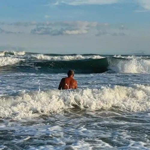 Person wading in ocean waves under a cloudy sky.
