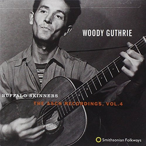 Black and white photo of Woody Guthrie playing an acoustic guitar.
