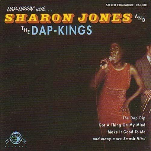 Sharon Jones singing into a microphone on a dark album cover with band members.