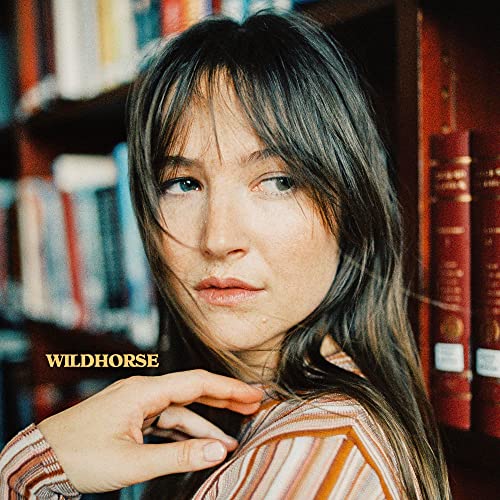 Close-up portrait of a woman with long dark hair, bookshelves behind.