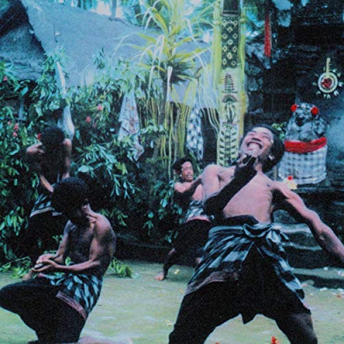 Men in traditional clothing dance outdoors amidst lush greenery.
