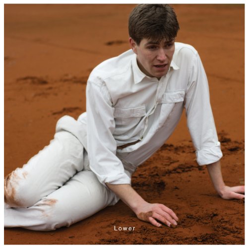 Man in white kneeling in reddish-brown sand, looking distressed.