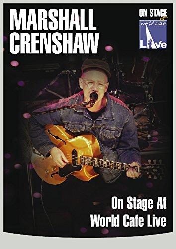 Marshall Crenshaw playing an electric guitar on a dark stage.