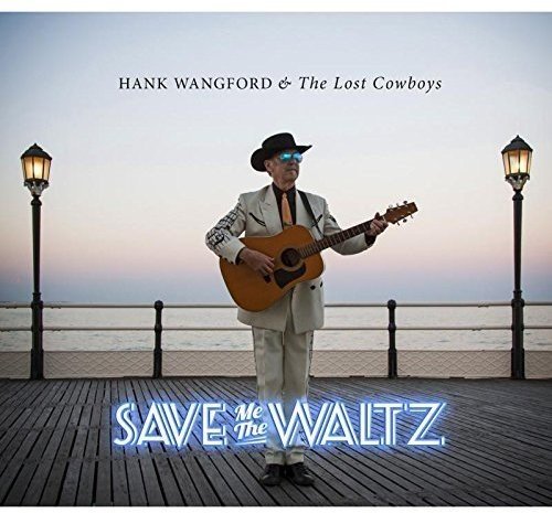 Hank Wangford playing acoustic guitar on a seaside pier.