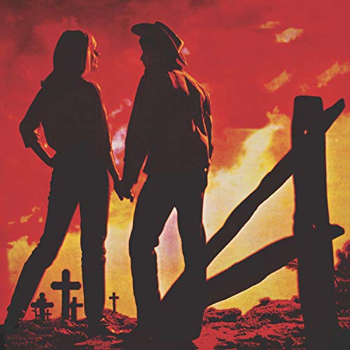 Silhouetted couple holding hands before a fiery, graveyard landscape.