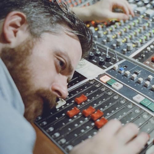 Man with beard operating a complex audio mixing console.
