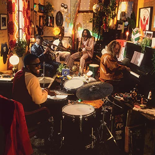 Ezra Collective band members playing instruments in a warmly lit, cluttered room.
